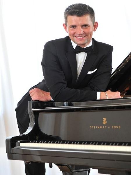 Schulleiter Besar Mitku über Steinway Flügel gebeugt